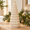 Neutral ceramic Christmas tree on an oak console with greenery and fairy lights; props not included