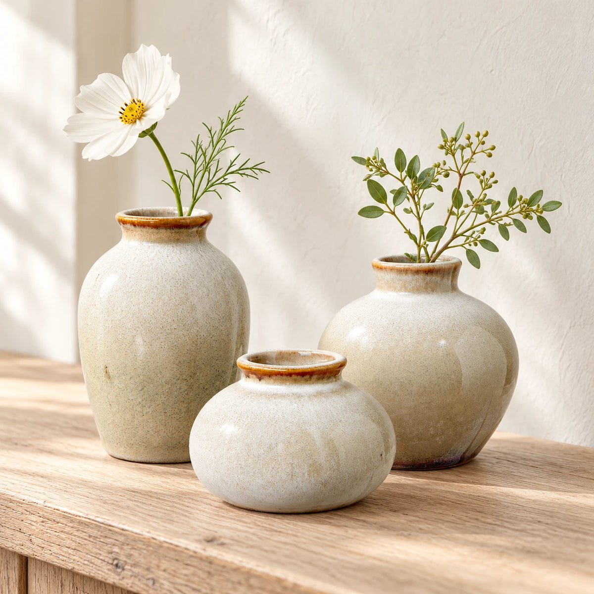 Three neutral ceramic mini bud vase sizes styled together on pale oak for comparison; each size is sold separately.