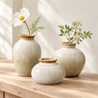 Three neutral ceramic mini bud vase sizes styled together on pale oak for comparison; each size is sold separately.