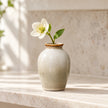 Large slim neutral ceramic mini bud vase with a single white flower on a cream kitchen shelf.