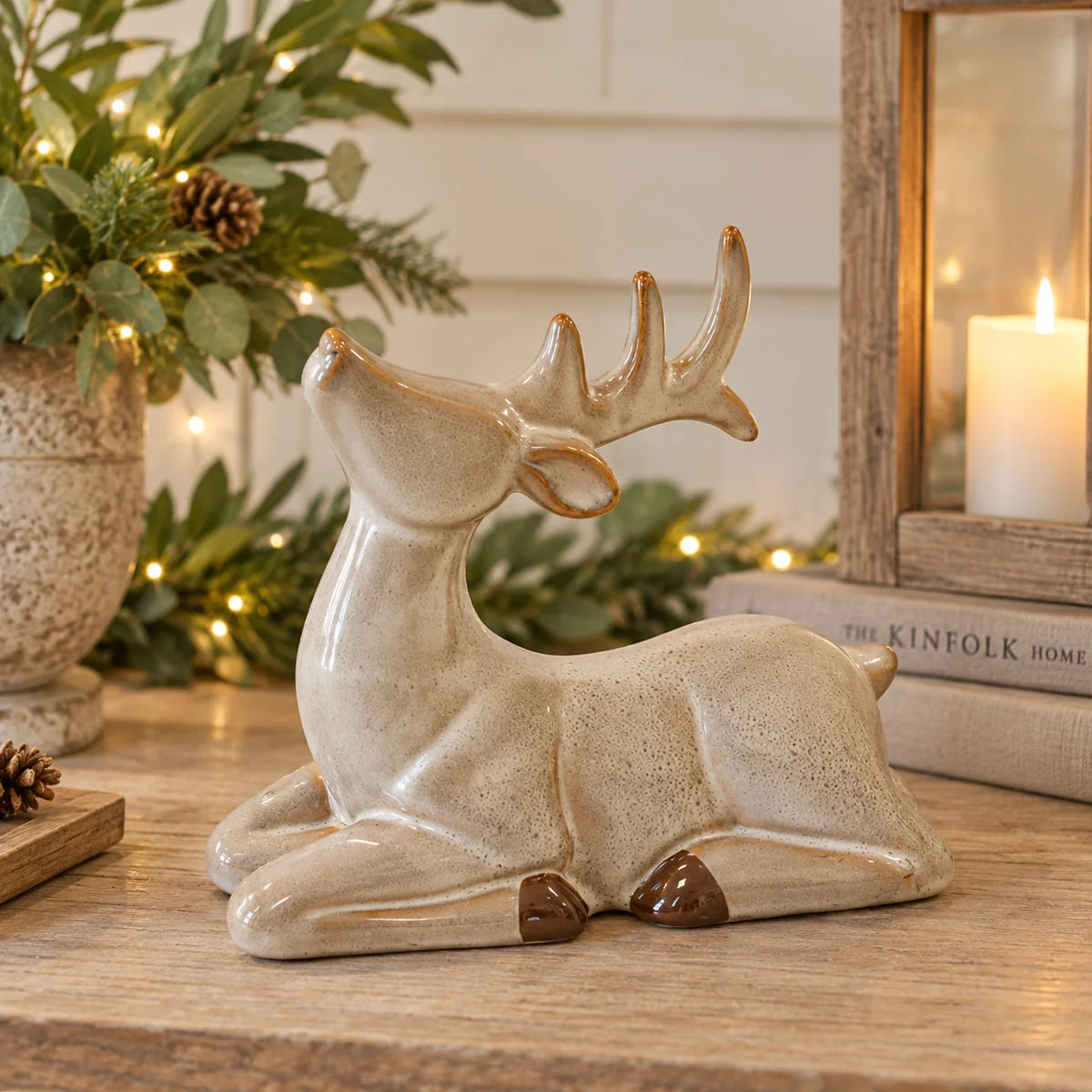 Neutral sitting ceramic reindeer with speckled glaze and brown hooves styled with Christmas greenery on rustic console