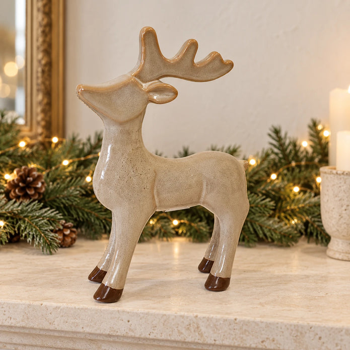 Standing ceramic reindeer ornament with brown hooves on a cream Christmas mantel.
