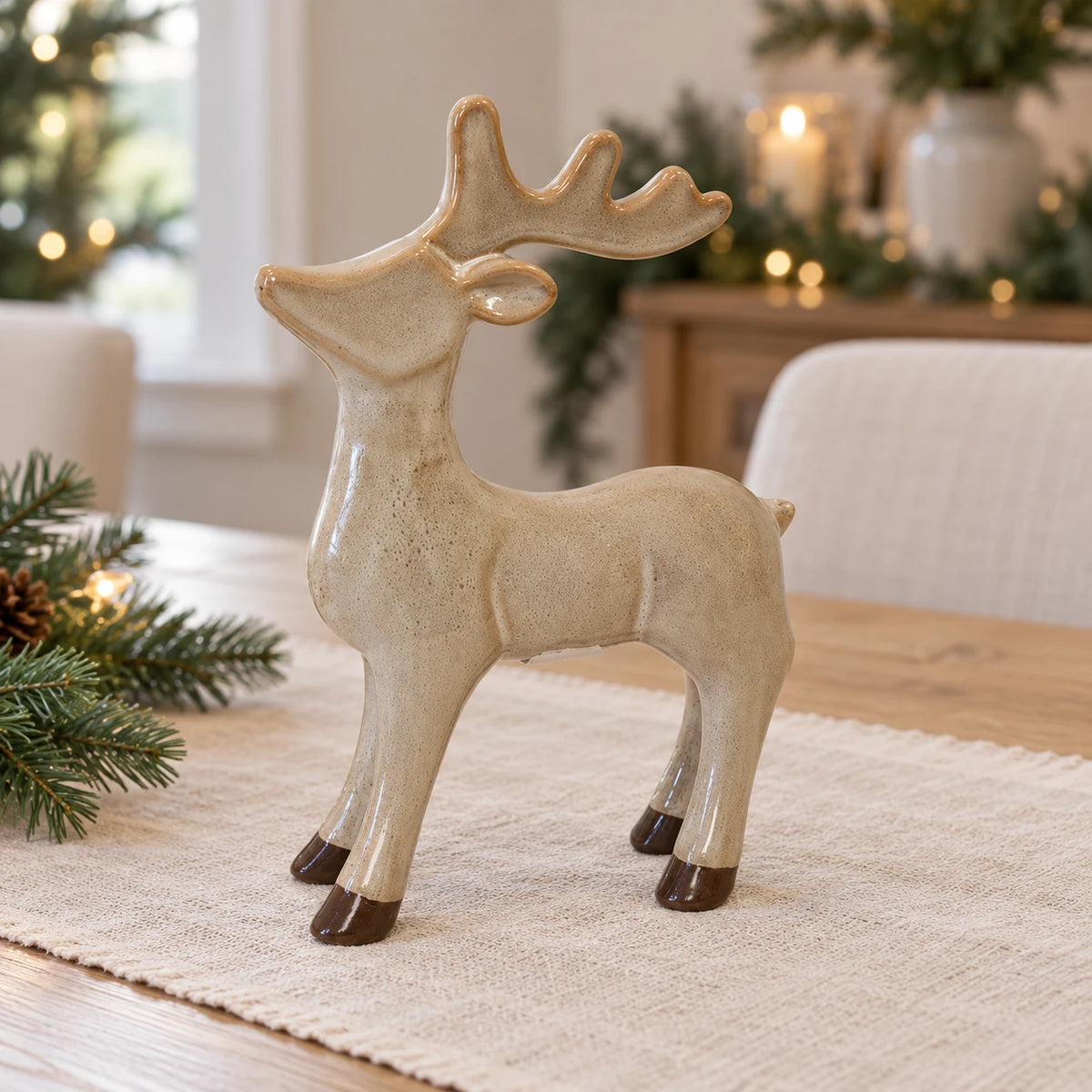 Neutral ceramic standing reindeer on a linen runner in a Christmas dining room.