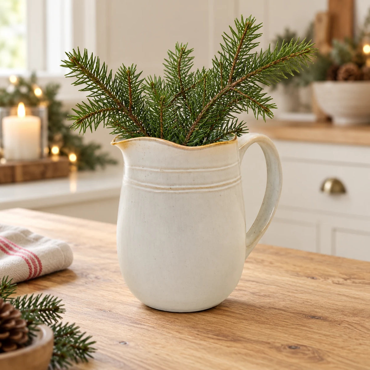 Cream stoneware jug holding faux fir stems on a country kitchen worktop