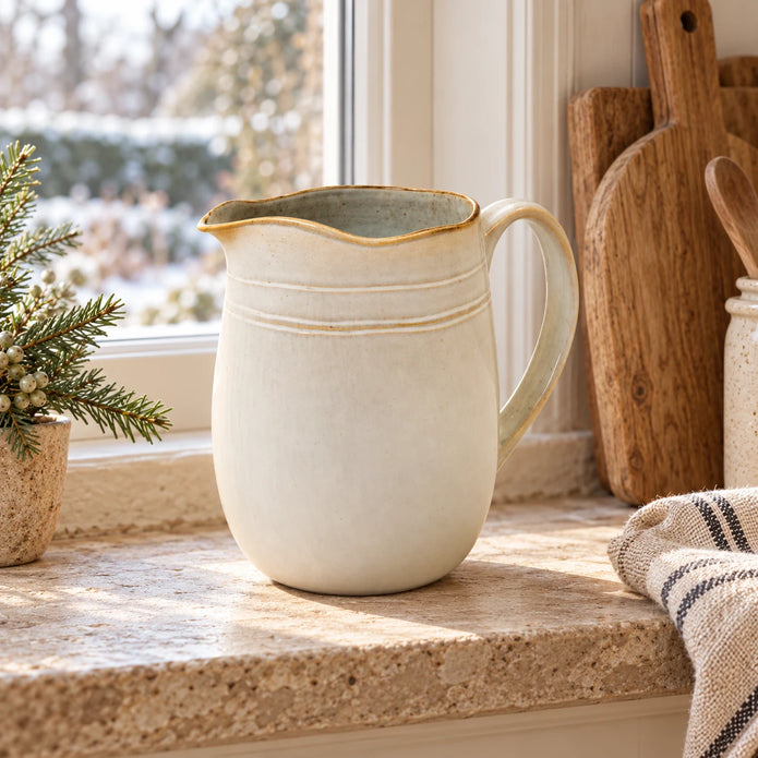 Cream stoneware jug on a country kitchen windowsill beside wooden boards