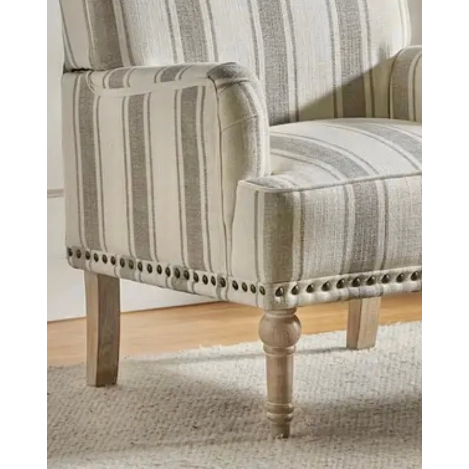 Close view of the beige striped armchair's arm, seat, nailhead trim and front wooden leg.
