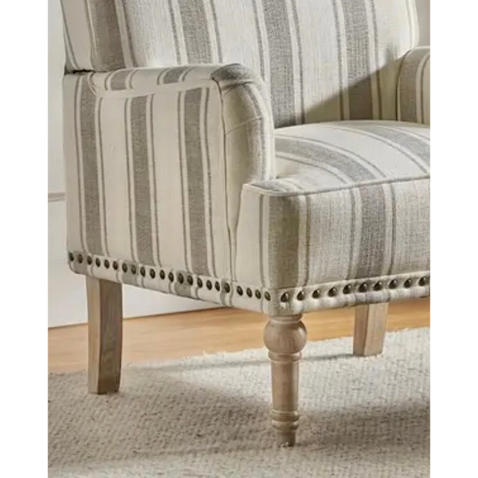 Close view of the beige striped armchair's arm, seat, nailhead trim and front wooden leg.