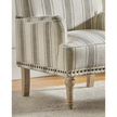 Close view of the beige striped armchair's arm, seat, nailhead trim and front wooden leg.
