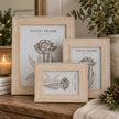 Three light whitewashed Isla wooden photo frames with floral inserts displayed together on rustic table