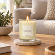 Heaven Scent Nutmeg, Orange + Cinnamon Medium Candle, lit in clear glass on a stone coaster in a living room