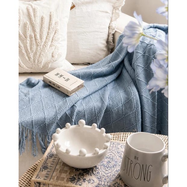 Ocean Blue Diamond Pattern Knitted Throw, blue knitted throw beside cream cushions and a book