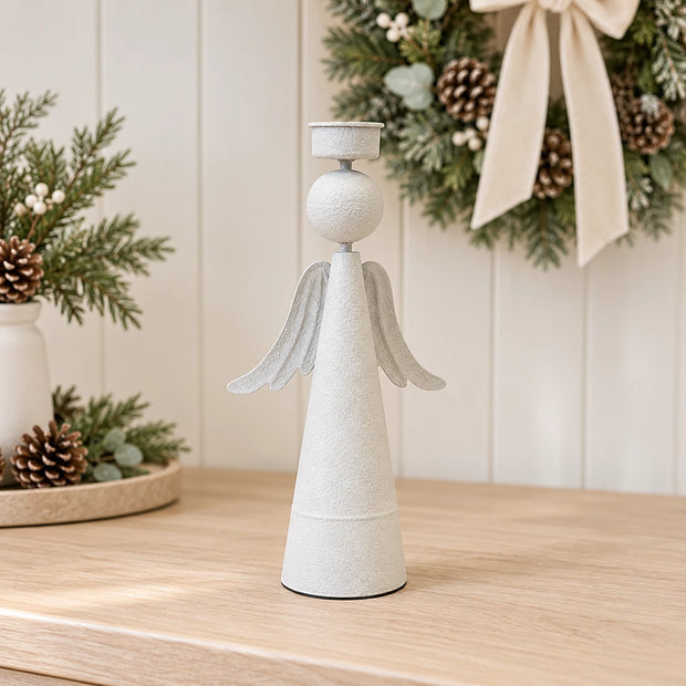 Empty off-white metal angel tealight holder on an oak console with a Christmas wreath and cream bow behind.