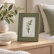 Olive green wooden Vilde photo frame styled on a bedroom bedside table with neutral furnishings