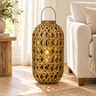 Large oval bamboo lantern styled with an LED candle prop beside a neutral linen armchair