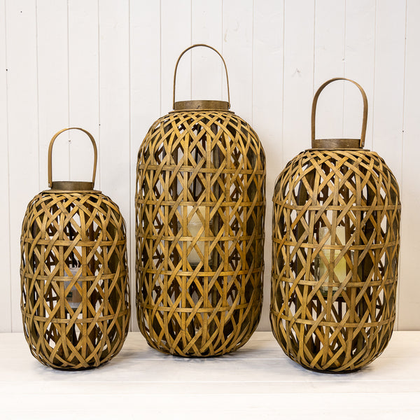Three oval bamboo lanterns with arched handles and glass inserts arranged on a white display shelf