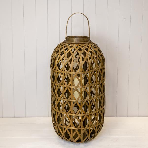 Oval bamboo lantern with a woven lattice, arched handle and glass insert on a white panelled shelf