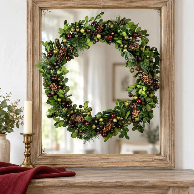 Pinecone and berry wreath hanging in front of an oak framed mirror
