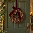 Pinecone wreath with burgundy bow hanging on a green cottage door