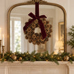 Pinecone wreath with burgundy bow centred on a mirror above a Christmas mantel