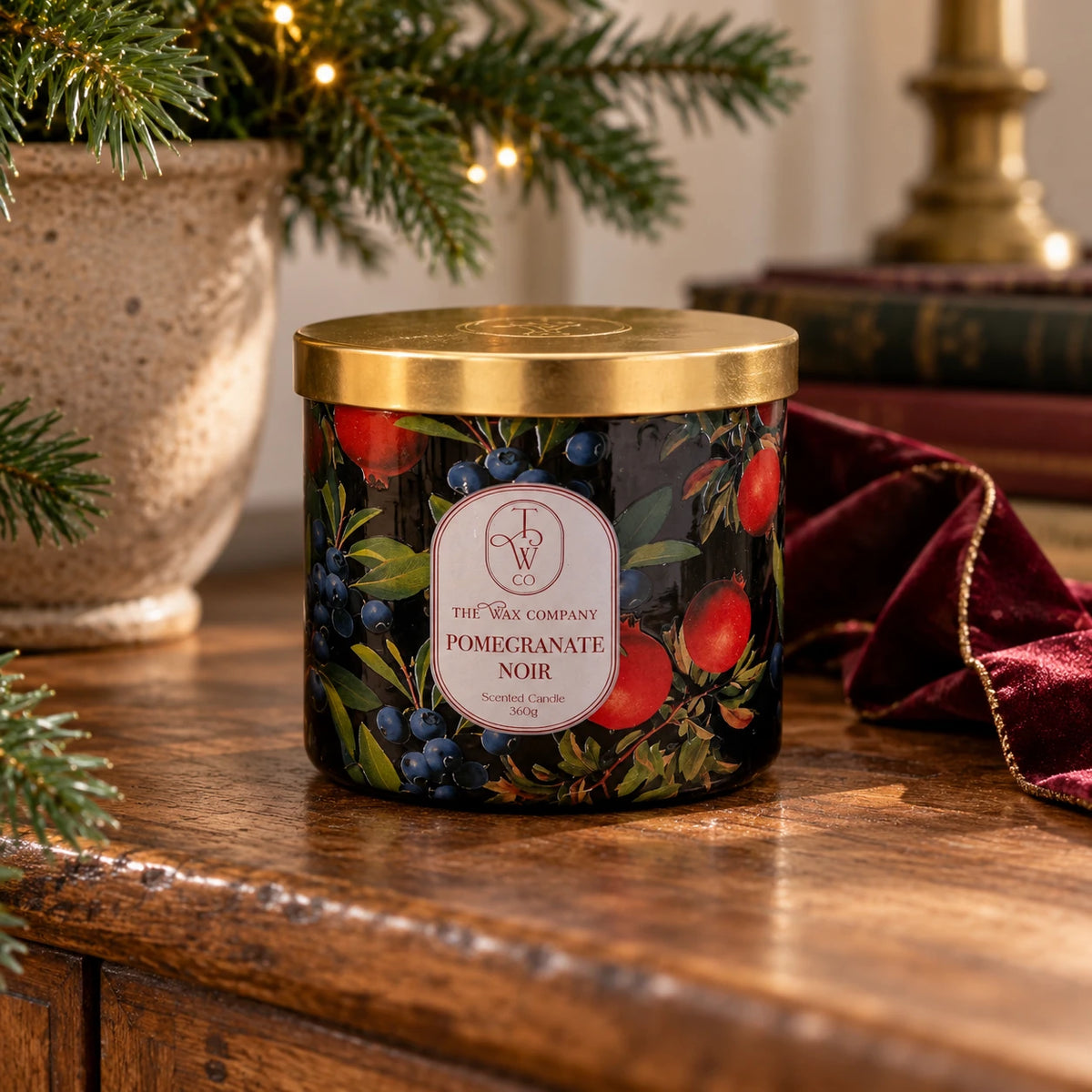 Pomegranate Noir candle with gold lid on an oak sideboard with Christmas greenery