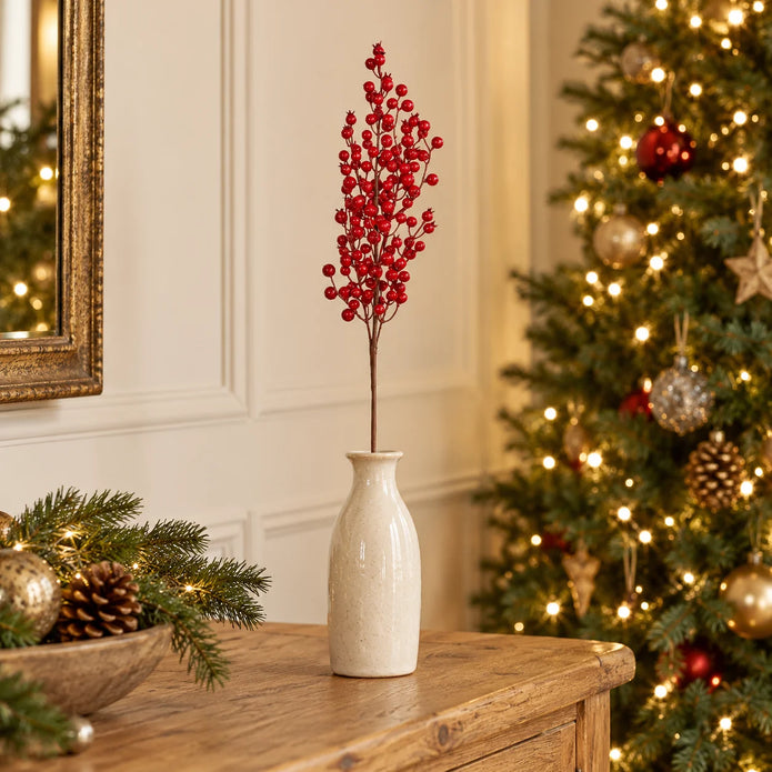 Single 60cm Red Berries Stem in a cream vase beside a Christmas tree