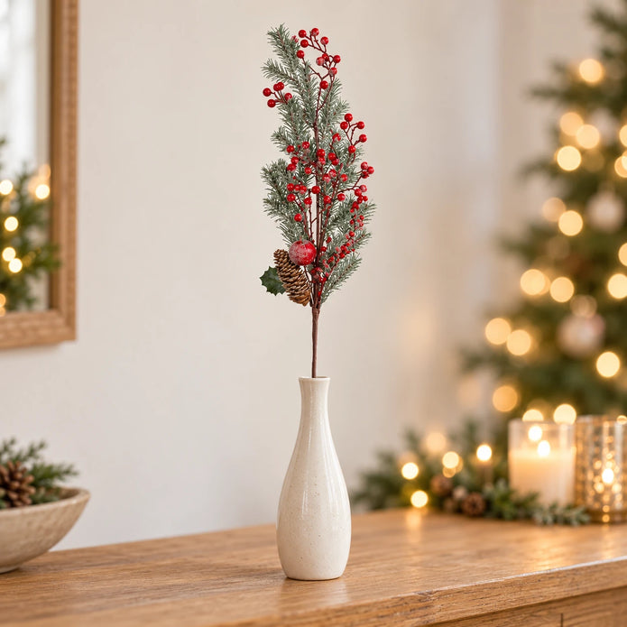 Single red berry and cedar festive stem in a cream vase on an oak console.