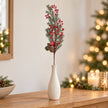 Single red berry and cedar festive stem in a cream vase on an oak console.