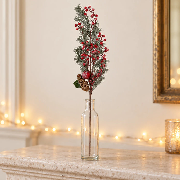 Red berry and cedar festive stem displayed in a clear glass bottle on a mantel.