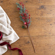 Full red berry and cedar festive stem laid on an oak table beside cream linen.