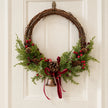 Large red berry twig Christmas wreath with pinecones, bell and bow, styled in a country Christmas door display