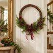 Large red berry twig Christmas wreath with pinecones, bell and bow, styled in a country Christmas hallway