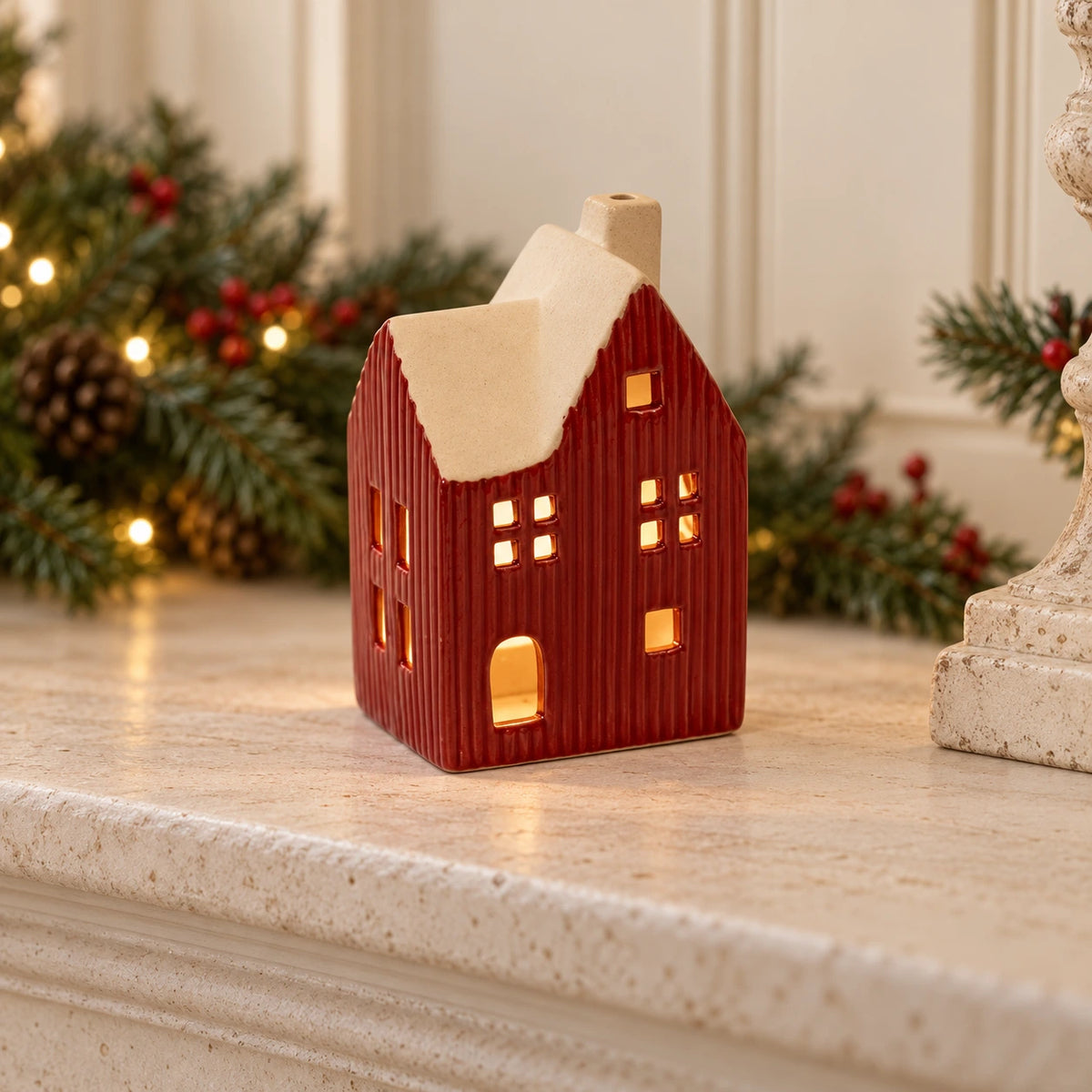 Red ceramic house tealight holder glowing on a Christmas mantel