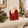 Red ceramic house tealight holder on a cream shelf with Christmas tree backdrop