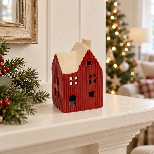 Red ceramic house tealight holder on a cream shelf with Christmas tree backdrop