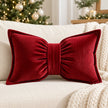 Red corduroy bow-shaped cushion styled on a cream sofa beside a Christmas tree and knitted throw.