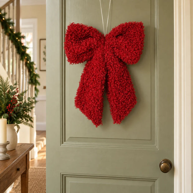 Red fluffy hanging bow on an olive cottage door.