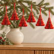Six red paper tree decorations with gold edges hanging from fir branches above an oak sideboard.