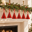 Six red paper Christmas trees suspended beneath a festive mantel garland.