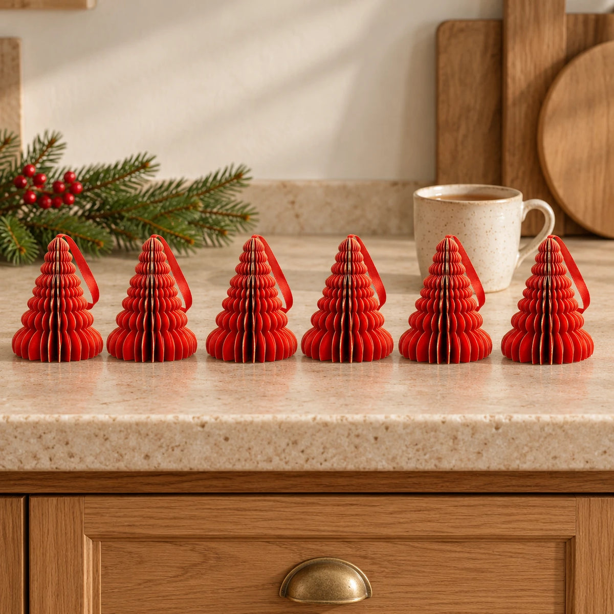 Six red paper tree ornaments on a kitchen counter with a mug of tea.