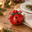 Small red Christmas bell with bow beside a linen napkin and white plate on an oak dining table