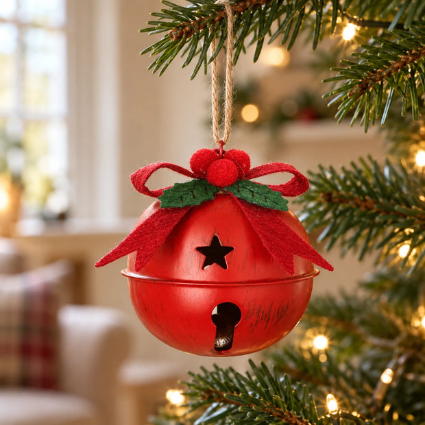 Small red metal bell with bow hanging from a Christmas tree branch in a warm country home