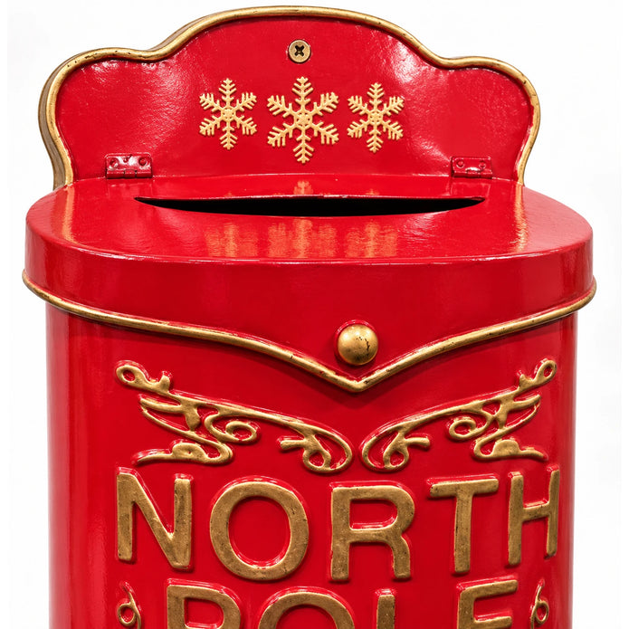 Close-up of the red metal Christmas letterbox showing three gold snowflakes, the letter slot, brass knob and raised gold lettering.