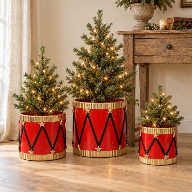 Set of three red metal drum planters holding small Christmas trees beside an oak console.
