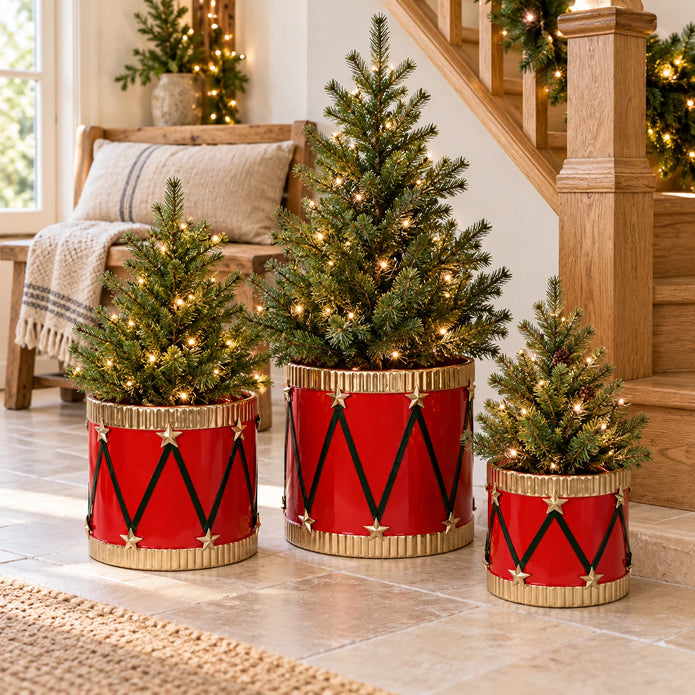 Red metal toy drum planters with small fir trees in a light country-home entrance.