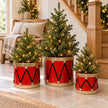 Red metal toy drum planters with small fir trees in a light country-home entrance.
