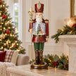 Red nutcracker LED snow globe on a stone surface beside Christmas greenery