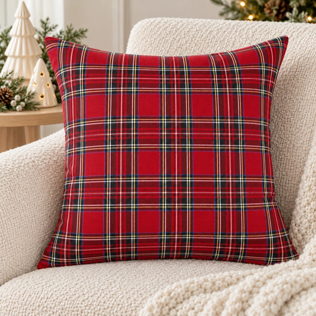 Red tartan check cushion cover on a cream boucle armchair beside ceramic Christmas trees