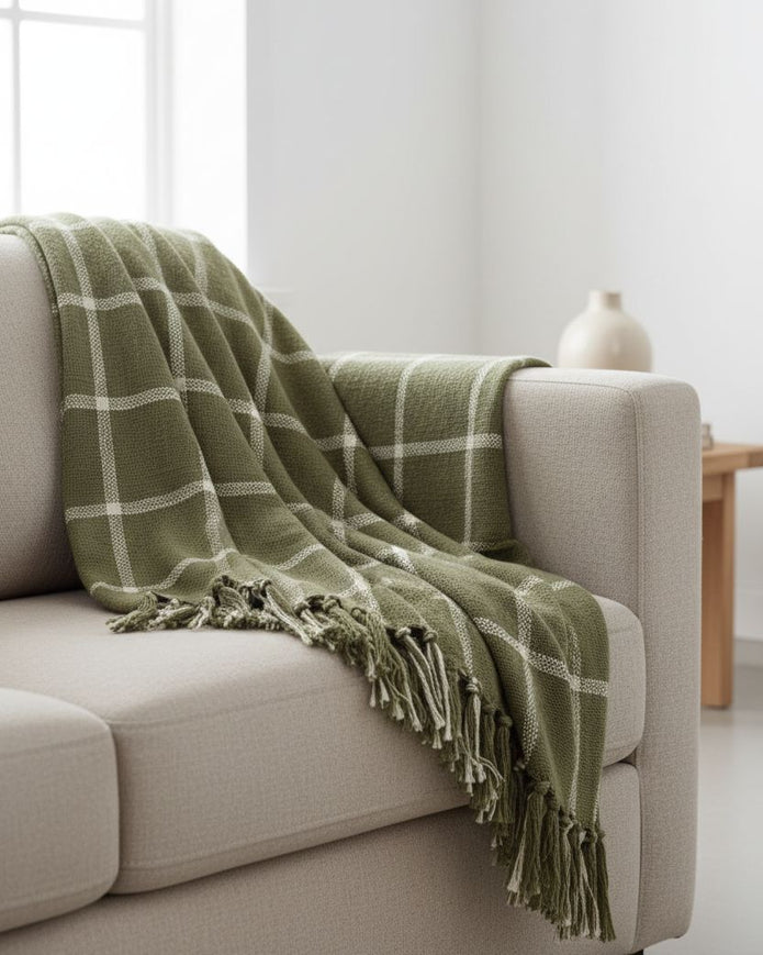 Green checkered blanket draped over a beige sofa in a bright living room.