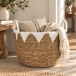 Round seagrass storage basket with white geometric trim and handles beside rustic console with folded textiles