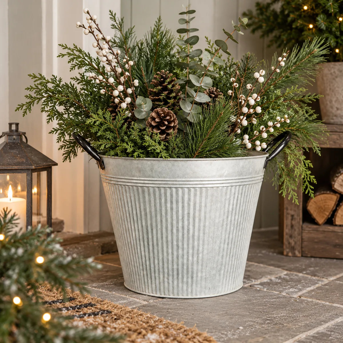 Round ribbed aged zinc planter with black handles styled with winter greenery and white berries on a sheltered porch